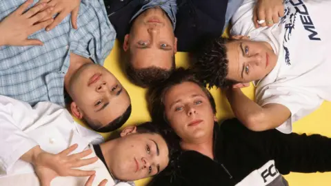 Getty Images A photo of the boyband Five in 1997 shows all seven members dressed casually, lying in a star formation on a bright yellow floor