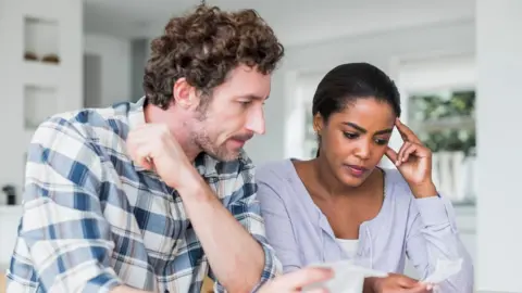 Getty Images A man and woman look at their bills at a kitchen table