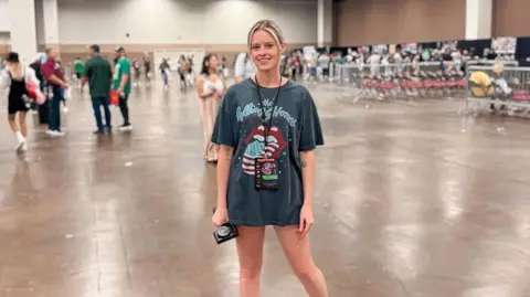 Chloe Webb Chloe s wearing an oversized Rolling Stones t-shirt and stood on a large convention floor.