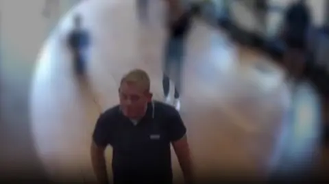 Thames Valley Police A CCTV image of Michael Jones, wearing a blue polo shirt, visiting Blenheim Palace, with figures in the background blurred