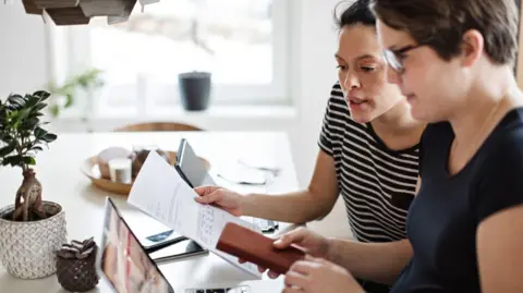 Getty Images Two women look at a bill while sitting at a desk.