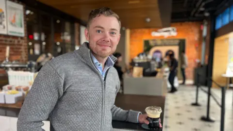 Capital One Shaun Rowley the director of Capital One cafes, holds a coffee as he smiles to the camera