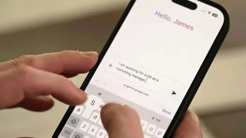 BBC A close-up of a smartphone showing the Gemini chatbot interface. At the top of the phone a greeting reads 