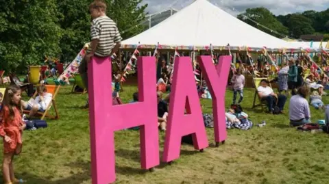 Getty Images The Hay-on-Why Festival in 2022. There is large pink letter spelling out Hay while a child sits on it. The letters are surrounded by festival-goers with a large white marquee in the background.