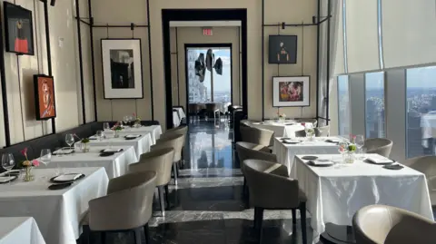 Rowan Bridge A row of tables and chairs with glasses and plates on top of them at American Express' Centurion New York venue