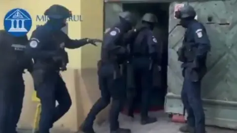 Romanian Police Armed Romanian police officers push down the door of a property wearing heavy protective gear.