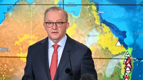 Reuters The Australian prime minister delivering a briefing in front of a screen showing weather warnings for the country's east coast