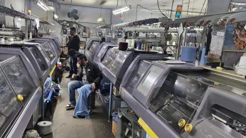 Nitin Goel The picture shows two men operating knitting machines at Consul Clothing's factory in Ludhiana city in India's north west. 