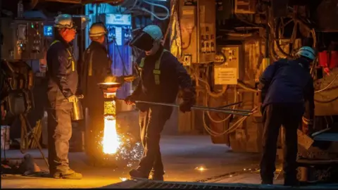 Getty Images Steel workers in Port Talbot, one carries a glowing pot of molten metal