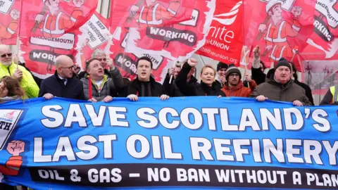 Andrew Milligan/PA Wire Workers gather behind a banner reading 'Save Scotland's last oil refinery' while holding placards