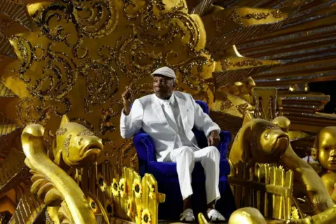 Antonio Lacerda / EPA Milton Nascimento, sitting on a float painted gold, waves to the crowd