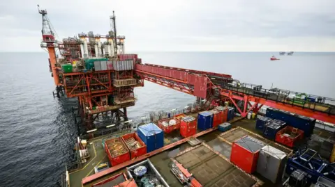 PA Media A general view of an oil rig. The structure is mainly red with a number of multi-coloured shipping crates on the deck.