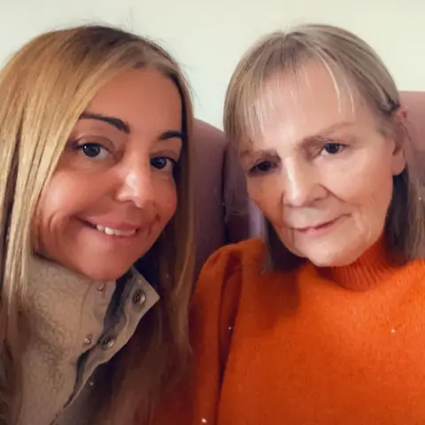 Nicola Hughes A selfie of Nicola with her mum Janette. Nicola is wearing a cream fleece and Janette is wearing an orange jumper. They are sitting on a pink couch.