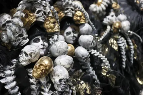 Andre Coelho / EPA Members of the Imperatriz samba school, their faces painted in white and black paint, are surrounded by plastic skulls, some painted white, others gold 