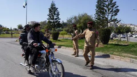 Reuters Syrian security forces speak with men on motorbike in Latakia, Syria (11 March 2025)