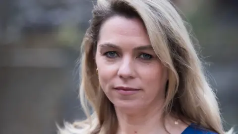 BBC Sarah Wynn-Williams - close up photo of an early-middle aged woman, who has long blond-light-brown hair. She is wearing make up and is looking directly at the camera. 