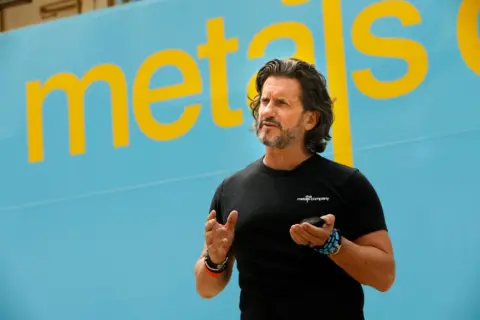 Getty Images Wearing a black t-shirt and multiple bracelets Gerard Barron stands beside a ship.