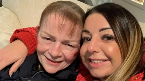 Nicola Hughes A selfie of Nicola Hughes (right) who has her arm around her mother Janette Ritchie. They are sitting on a cream couch and smiling at the camera.