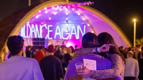 Getty Images Survivors of the Nova festival, bereaved friends and family and invited guests pictured at a memorial for the victims of the attack which was held in November 2023. The picture shows a crowd looking towards a tent with neon lighting spelling out the words 