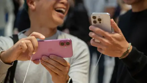 Getty Images Customers hold Apple iPhone 16 and 16 Pro in a shop