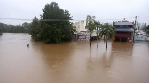 Getty Images Brown floodwater swamps a main road in Lismore, with the water reaching metres high up buildings and trees