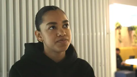 A woman with black hair and wearinga black hoodie looking off-camera