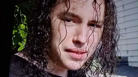Family handout Vlad Nikolin-Caisley looks at the camera through his long, curly and black hair which hangs down to his shoulders. He is wearing a black t-shirt.