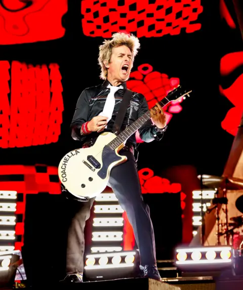 Getty Images Billie Joe Armstrong of Green Day pulls a face while strumming a white electric guitar.